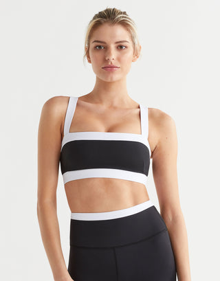 Woman wearing a black and white sports bra and leggings on a light gray background