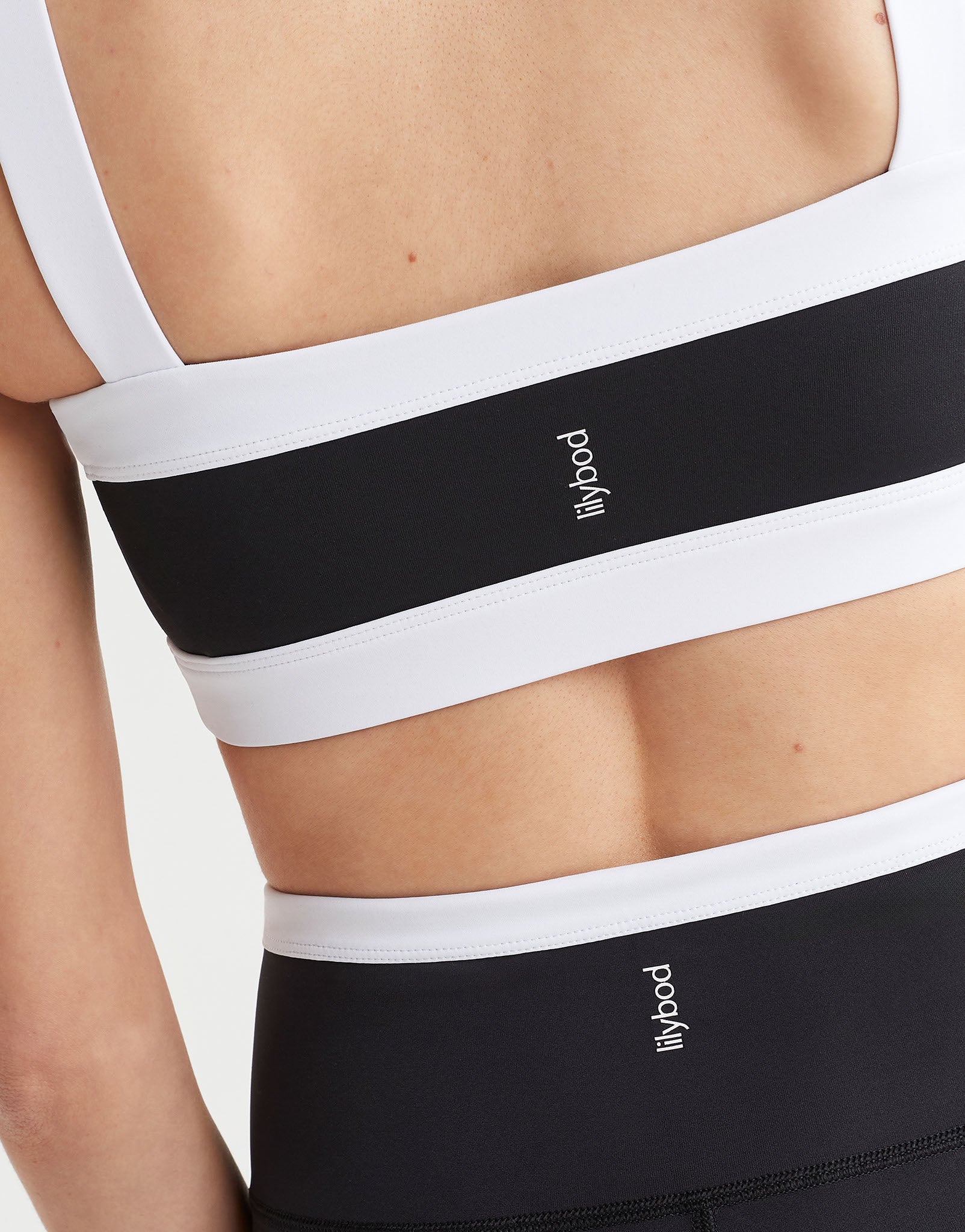 A model wearing a black and white sports bra with a bandeau style silhouette and the Lilybod logo at the center back.