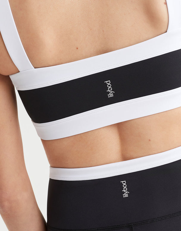 A model wearing a black and white sports bra with a bandeau style silhouette and the Lilybod logo at the center back.