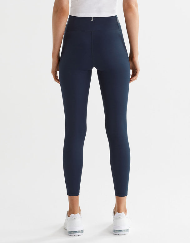 A woman wearing navy and white high-waisted leggings with a color-blocked waistband and a printed accent pattern on the legs. She is also wearing a white sports bra and white sneakers.