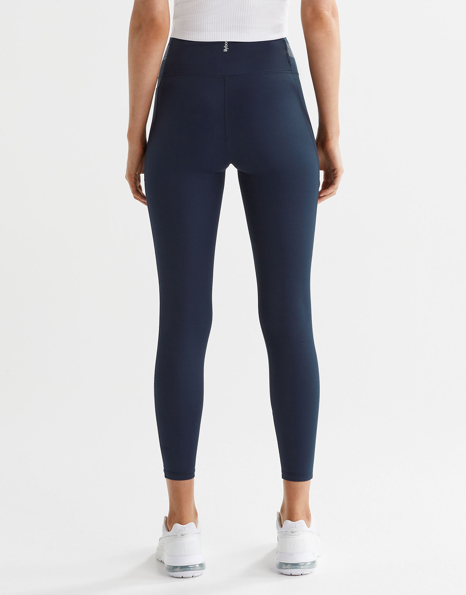 A woman wearing navy blue sporty leggings with white runners on a white background.