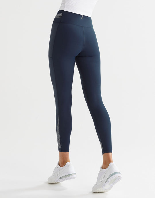 A model wearing navy and white high-waisted leggings with a color-blocked waistband and a printed accent pattern on the legs.