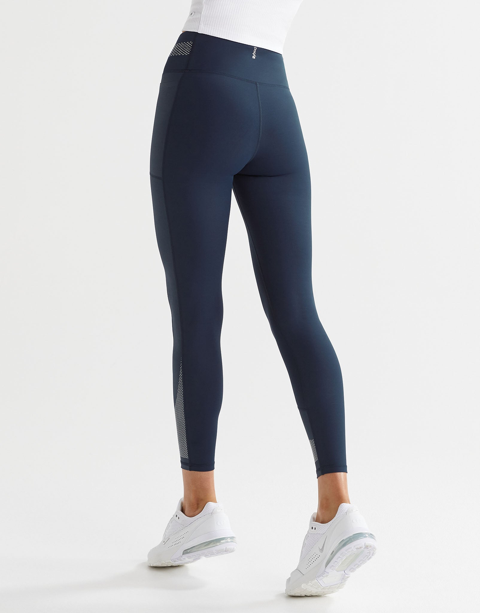 A woman wearing navy blue sporty leggings with a white top and white runners.