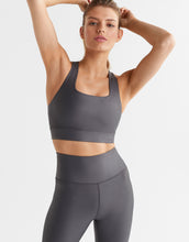A model wearing a shiny grey sports bra and leggings.