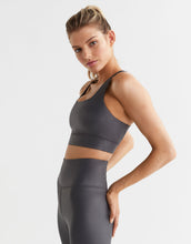 Woman wearing a gray sports bra and leggings on a light gray background