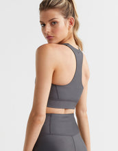 Woman wearing a gray sports bra and leggings on a light gray background