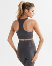 A model wearing a shiny wet look grey sports bra and leggings.