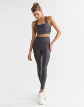 A model wearing a shiny grey sports bra and leggings and white runners.