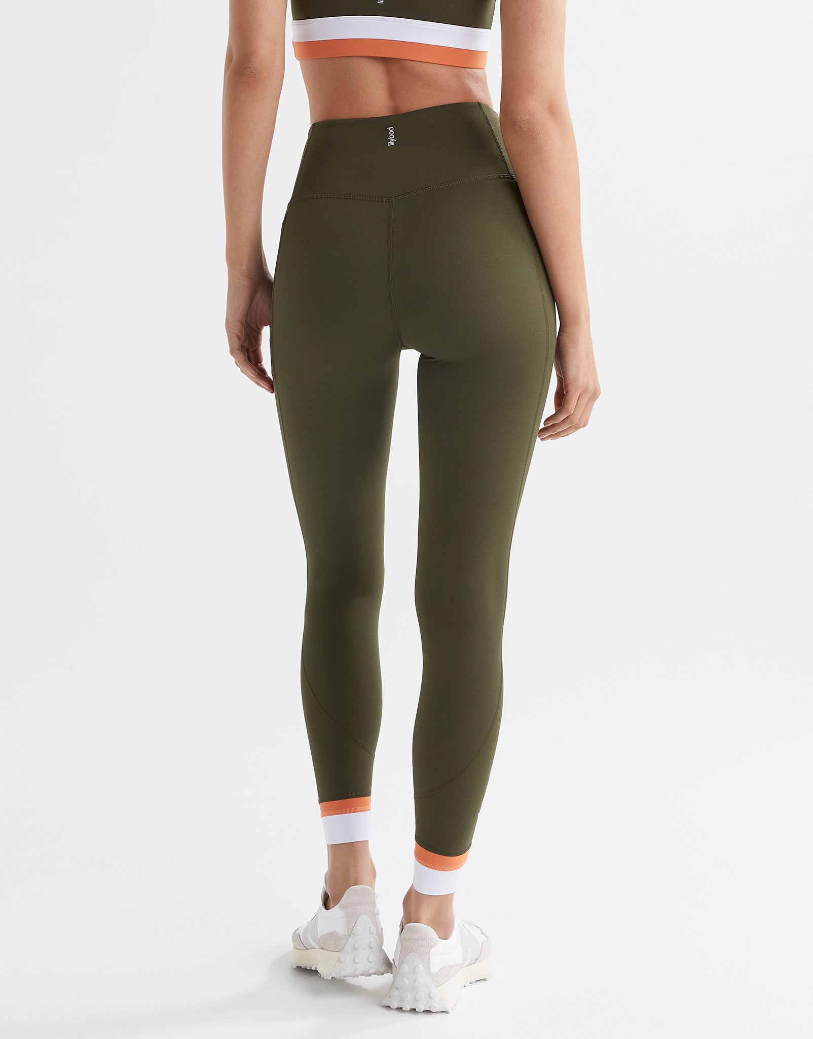 A woman wearing army green leggings with a white and orange cuff on the leg.