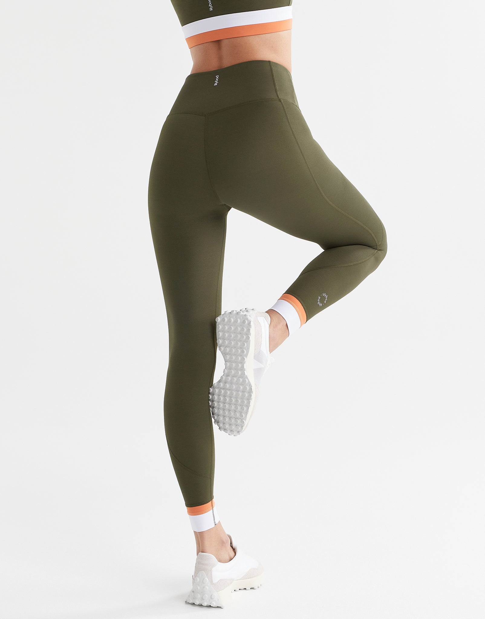 A woman posing wearing army green leggings with a white and orange cuff.