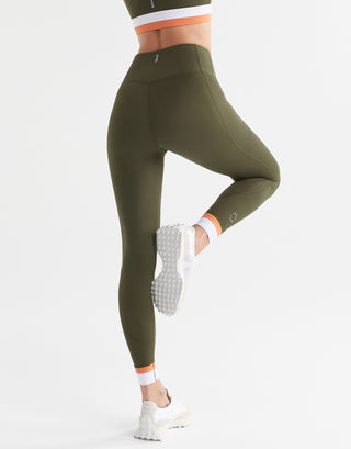 A woman posing wearing army green leggings with a white and orange cuff.