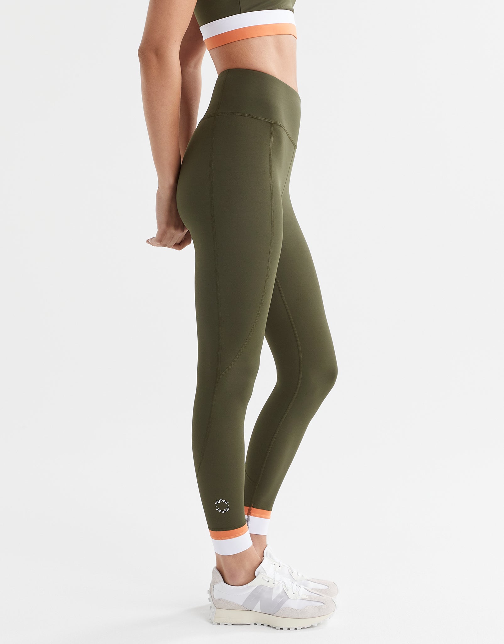A woman wearing army green leggings  and a matching sports bra with a white and orange cuff.