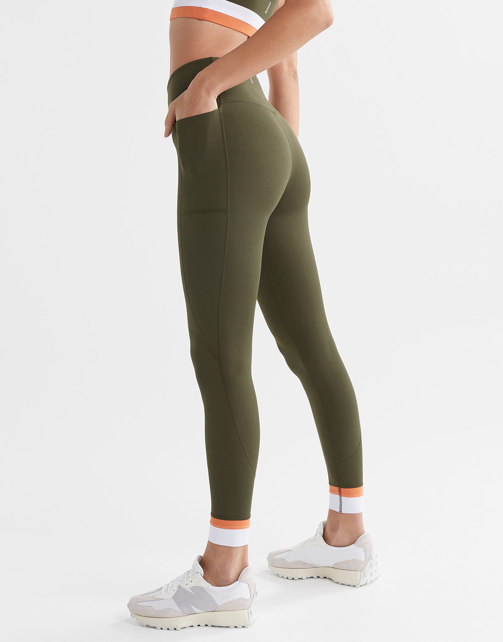 A woman wearing army green leggings with a white and orange cuff and white runners.