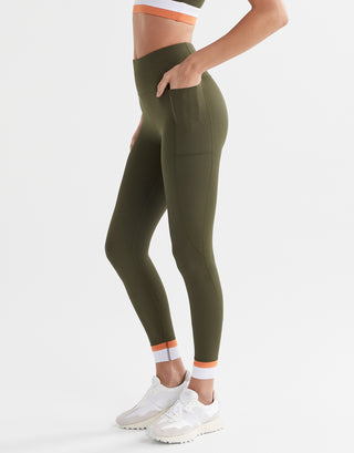 A woman wearing army green leggings with pockets and a white and orange cuff.