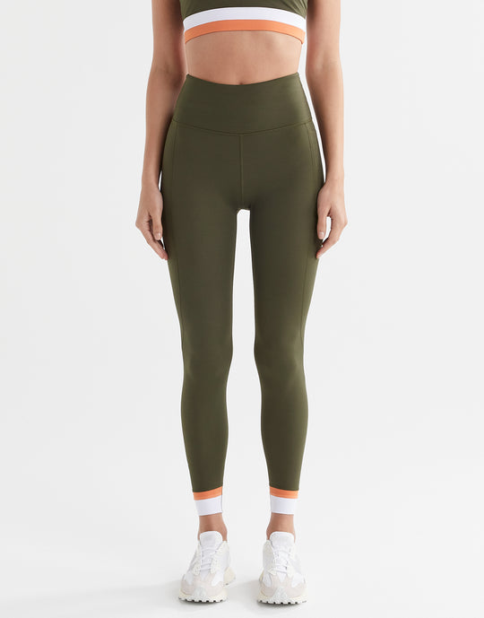 A woman wearing army green leggings with a white and orange cuff.