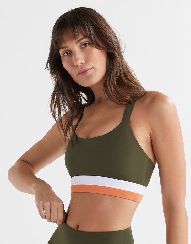 A woman wearing an olive green sports bra with white and orange color blocks on the underband.