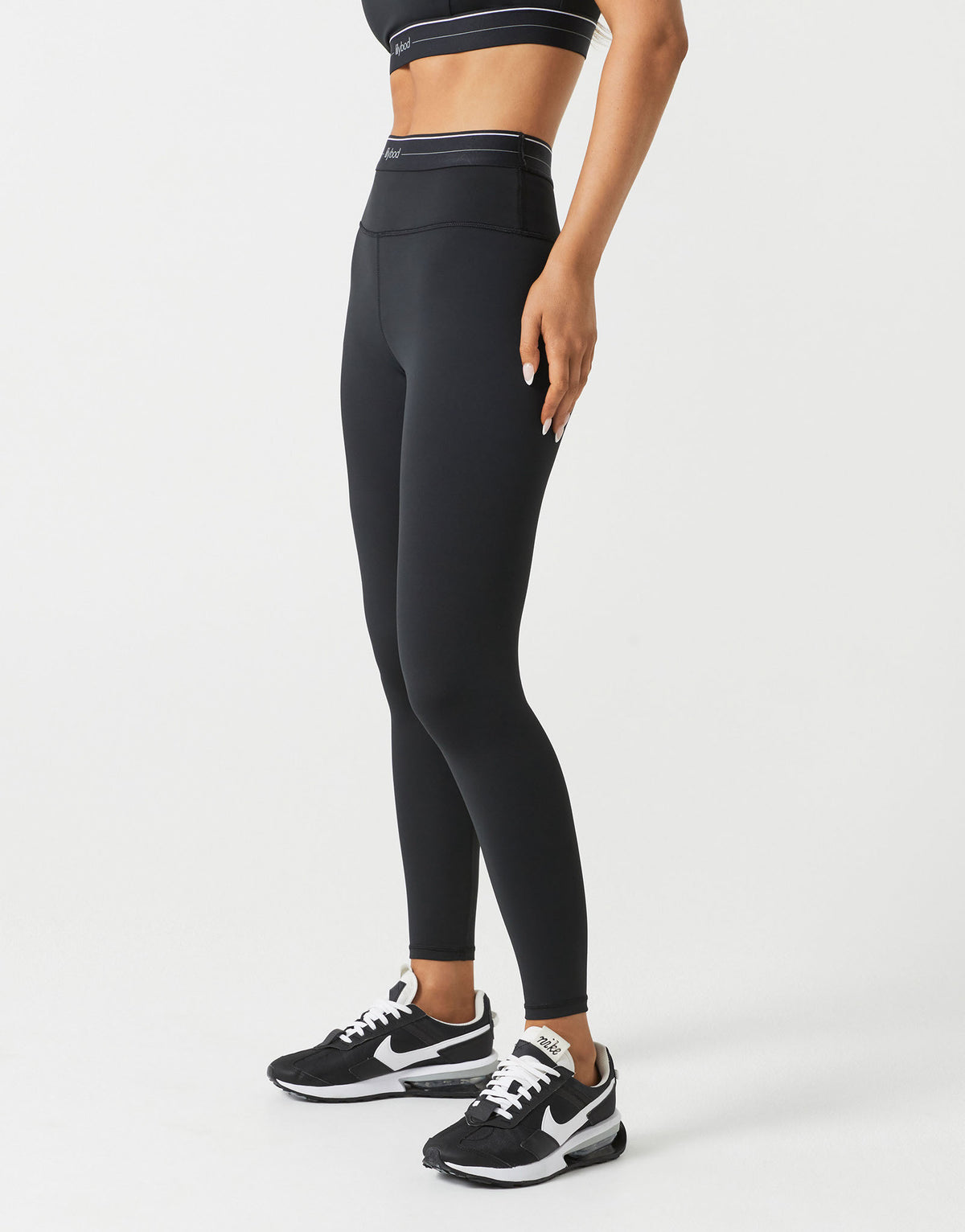 A woman wearing black leggings and a top on a white background.