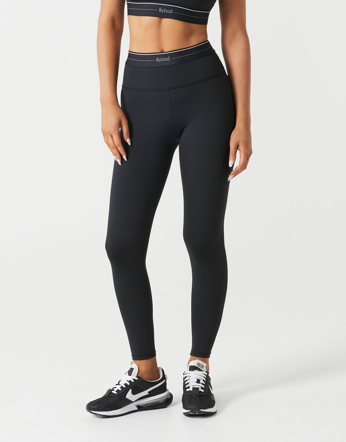 A woman wearing black leggings and runners on a white background.