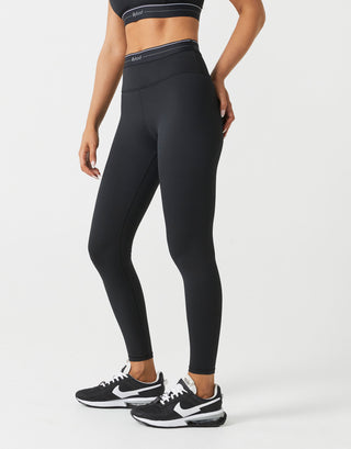 A woman wearing black leggings and a black top on a white background.