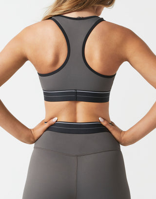A model wearing gray leggings and a racerback sports bra on a white background.