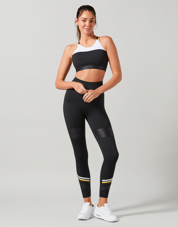 Woman wearing a black sports bra and leggings with white sneakers on a gray background
