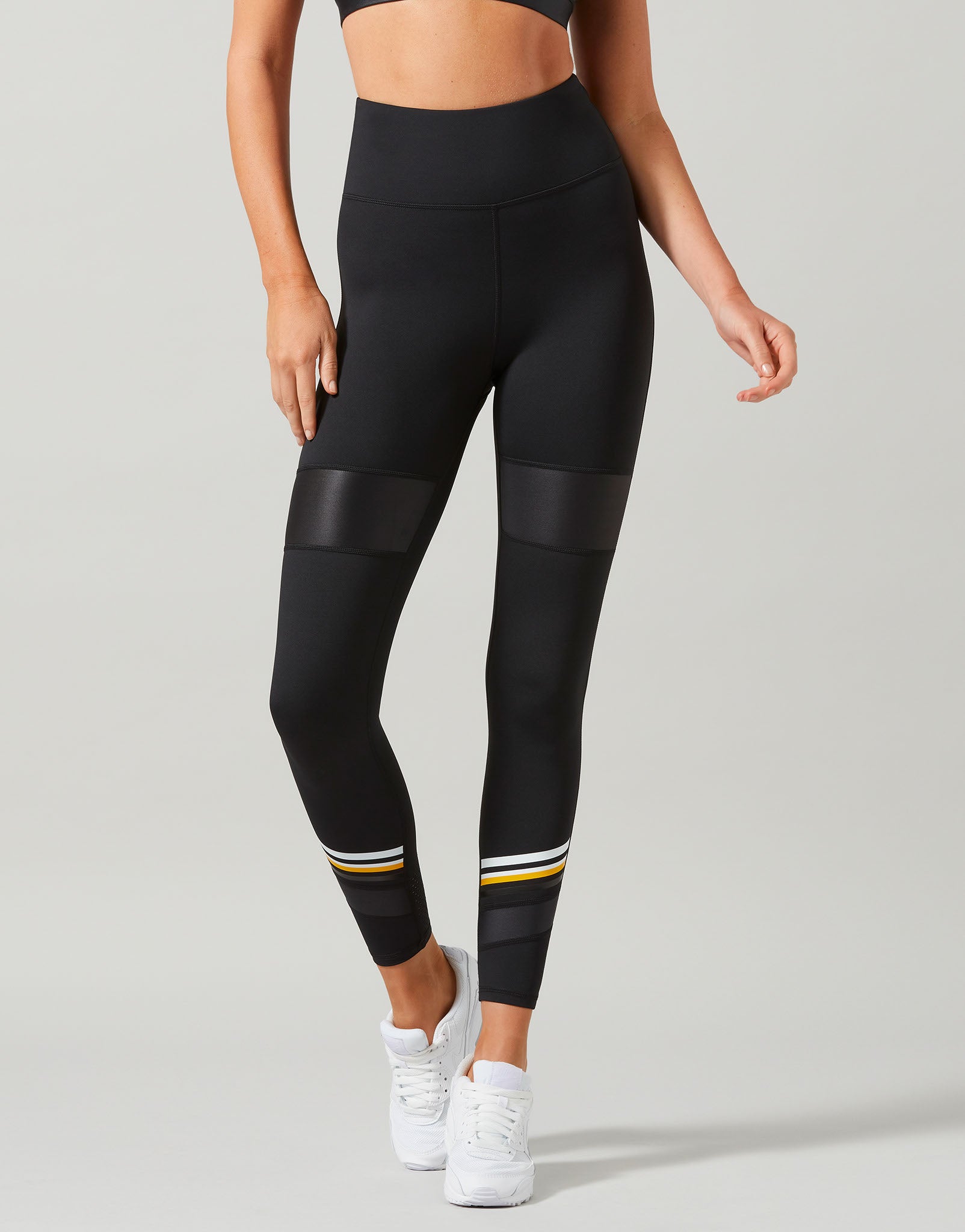 Person wearing black leggings with yellow accents on a gray background