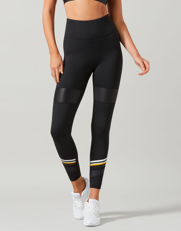 Person wearing black leggings with yellow accents on a gray background
