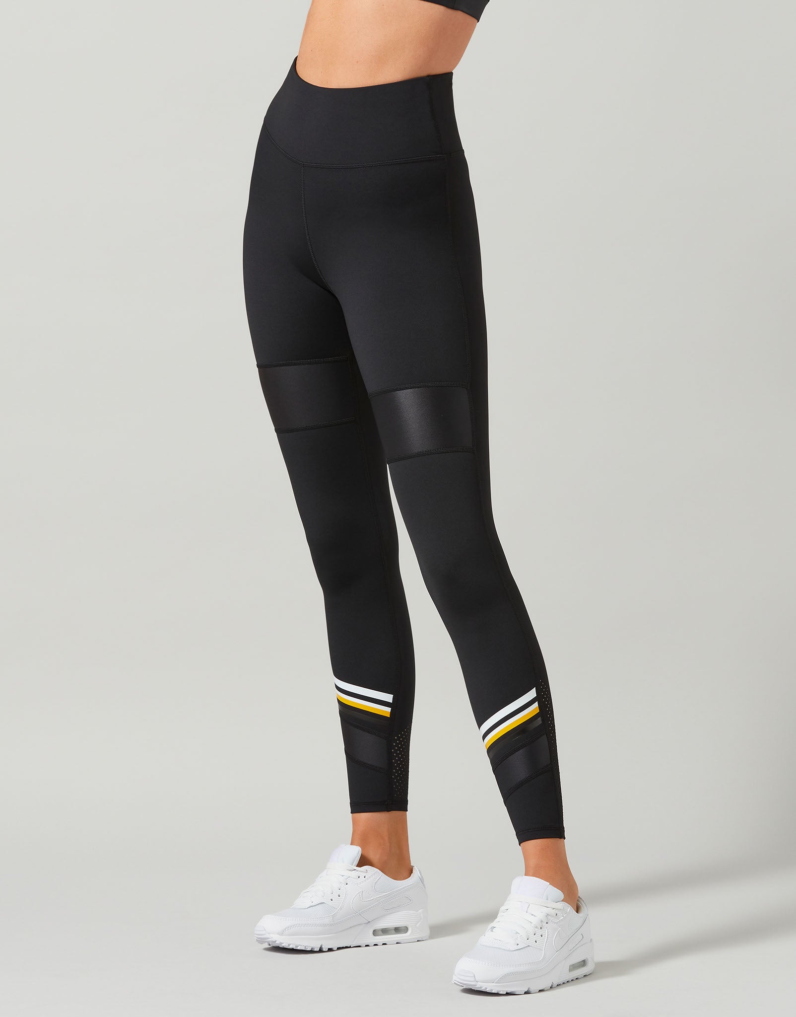 Black leggings with patchwork design and white sneakers on a gray background