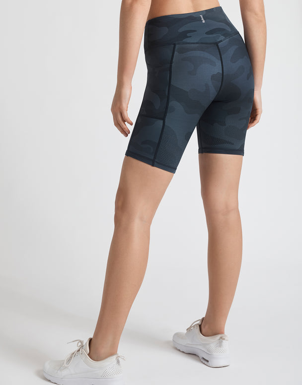 A woman wearing navy blue camo bike shorts and white runners.