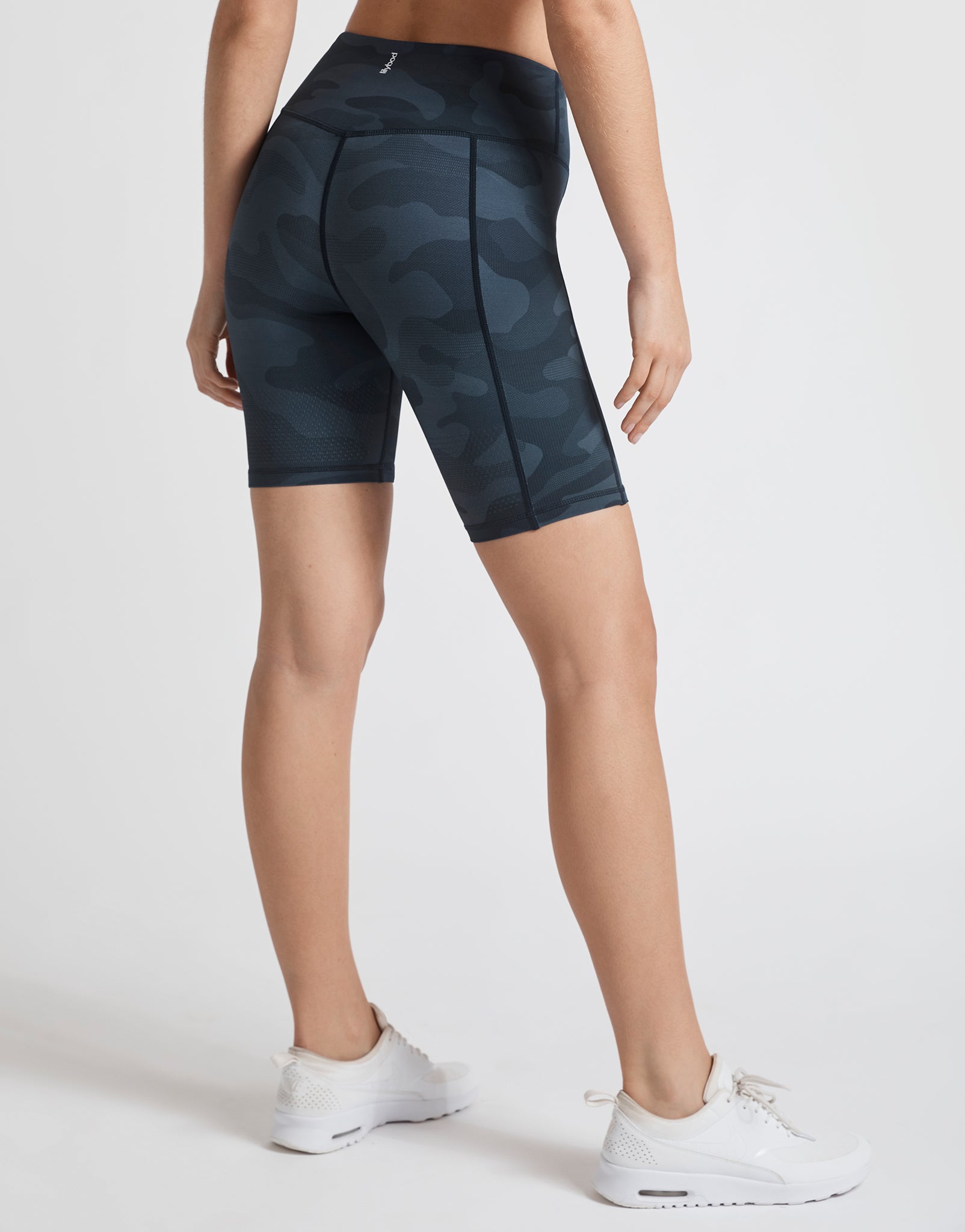 A model wearing dark blue camo bike shorts and white runners.