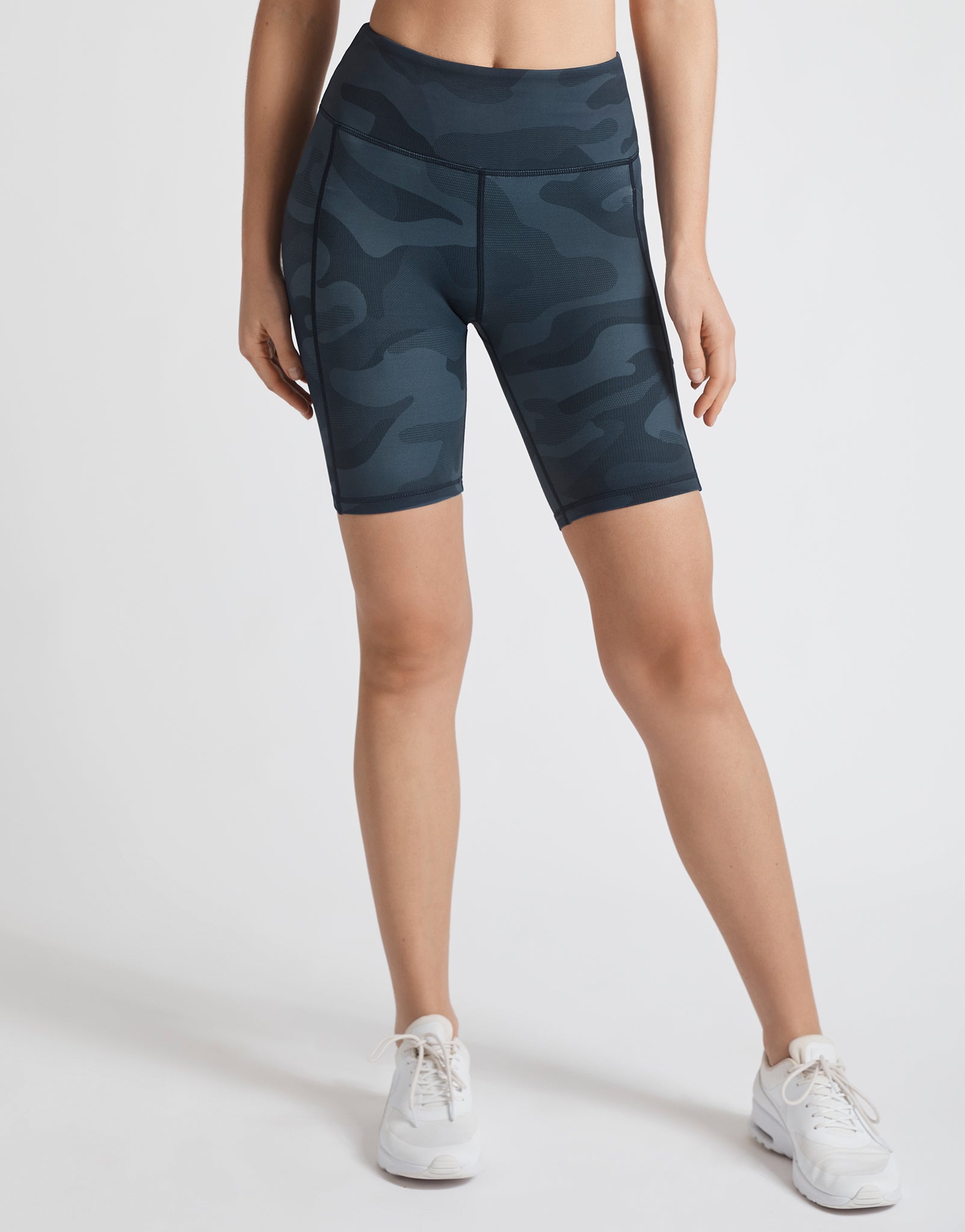A model wearing navy blue camo bike shorts and white runners.