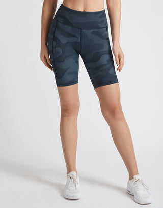 A model wearing navy blue camo bike shorts and white runners.