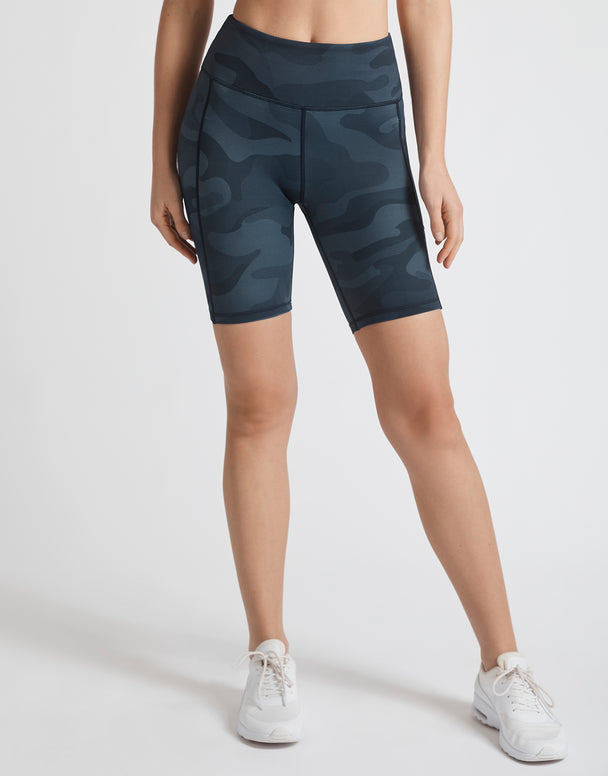 A model wearing navy blue camo bike shorts and white runners.