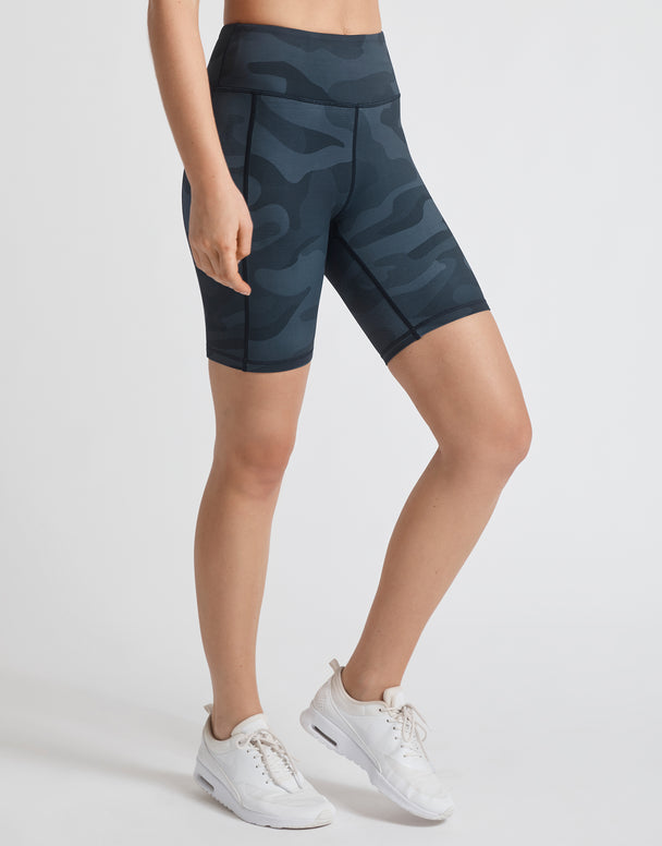 A model wearing navy blue camo high waist bike shorts and white runners.