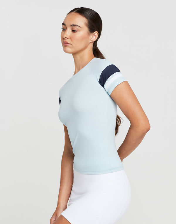 Woman wearing a light blue t-shirt with dark blue and white sleeves against a plain background