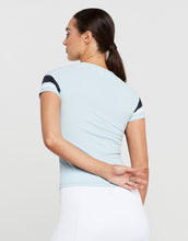 Woman wearing a light blue top with black and white sleeves on a plain background