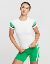 Woman wearing a white and green athletic t-shirt and shorts on a light grey background