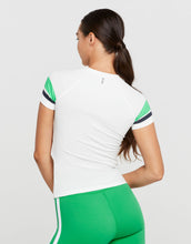 Woman wearing a white and green athletic t-shirt and shorts on a plain background