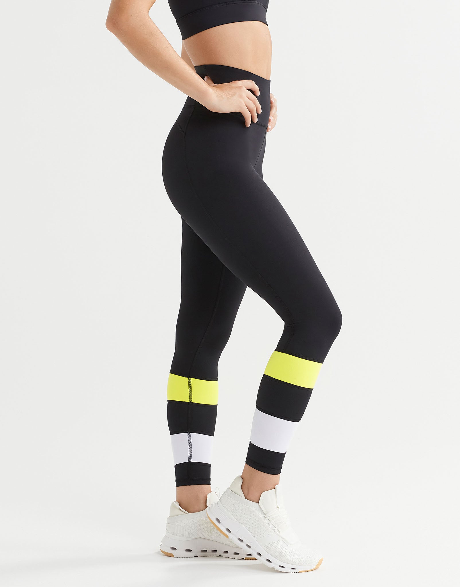 Person wearing black leggings with yellow and white accents on a white background