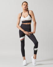 Woman wearing a black and white sports bra and leggings set on a gray background