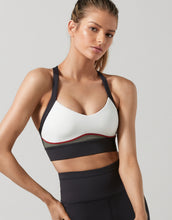 Woman wearing a white sports bra with black straps on a gray background