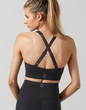 Woman wearing a black sports bra with criss-cross straps on a light gray background