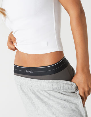 A close up of a woman wearing a white tank top and grey sweatpants.