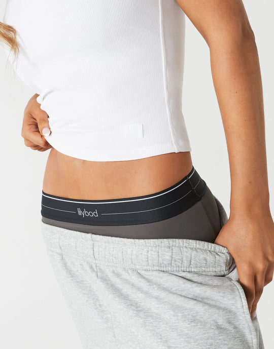 A close up of a woman wearing a white tank top and grey sweatpants.