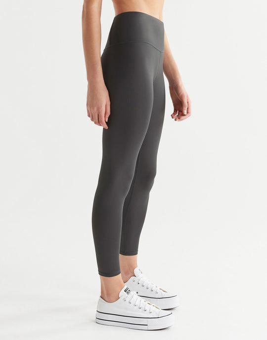 A pair of high shine gunmetal colored leggings, featuring minimal seaming and a logo at the center back. The leggings are presented in a standing position on the side.