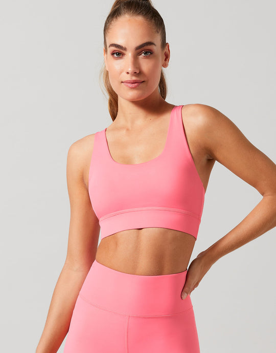 A woman wearing a pink sports bra and matching leggings, posing with one hand on her hip.
