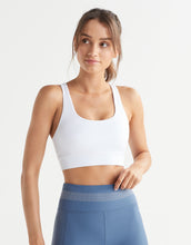 A woman wearing a white sports bra and blue leggings on a white background