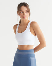 Woman wearing a white sports bra and blue leggings on a light gray background