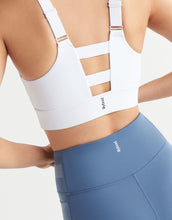 A close up of a woman wearing a white sports bra and blue leggings on a white background