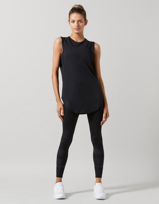 Woman wearing a black sleeveless top and leggings on a gray background